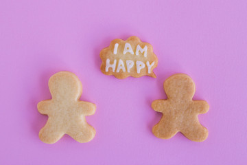 Homemade shortbread cookies with white glaze on pink background, top view. Two people with callout cloud with text ‘I am happy’