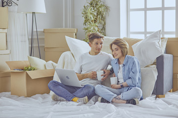 Portrait of happy couple looking at laptop computer together sitting in new house, surrounded with boxes