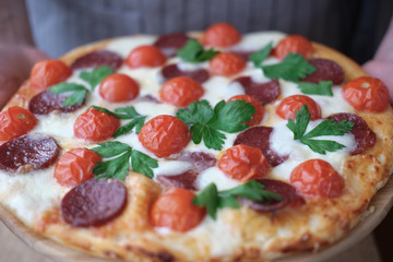 homemade pizza, italian traditional pepperoni pizza made with cherry tomatoes, mozzarella and and salami. fresh baked pizza in human hands.