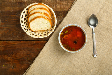 cup of italian tomato soup with potatoes and mushrooms on a wooden table on a napkin and a spoon and bread.
