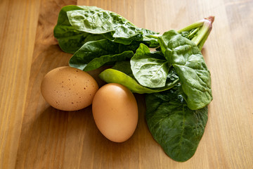 Fresh spinach leaves and brown chicken eggs isolated on a wooden table