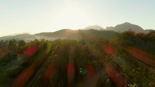 Aerial shot of trees and mountains against sky during sunrise, drone descending over landscape - Tat Sae Waterfalls, Laos