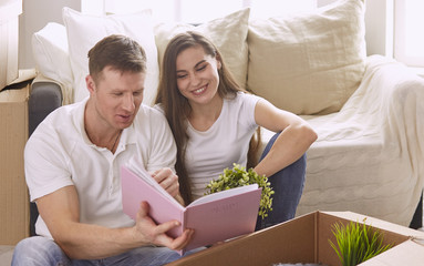 Portrait of happy couple looking at laptop computer together sitting in new house, surrounded with boxes