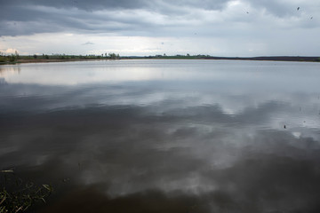dark rain clouds hang low in the sky and reflected in the lake