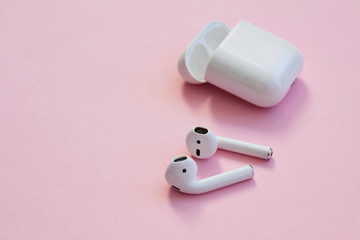 White wireless headphones are on a pink background.