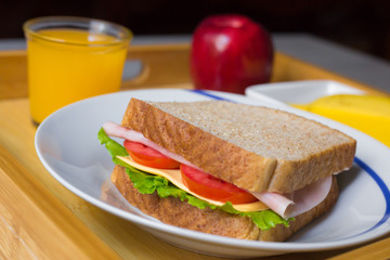 Close-up of breakfast made with a ham sandwich, orange juice, a banana and an apple on a wood plate over the table