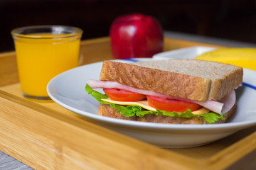 Close-up of breakfast made with a ham sandwich, orange juice, a banana and an apple on a wood plate over the table