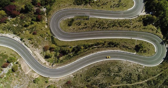 Yellow sports car driving along hairpin bends in valley