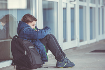 Little boy or child sitting alone on floor in front of the school after suffering an act of bullying