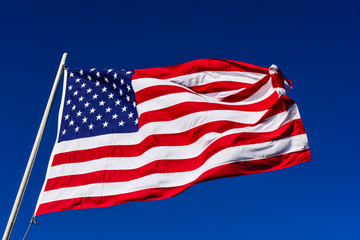 American flag is flowing in the wind on blue sky background.