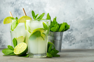 Two homemade lemonade or mojito cocktail with lime, mint and ice cubes in a glass on a light stone table. Fresh summer drink. With copy space.