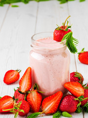 Strawberry cocktail in a glass jar on a wooden white table. Strawberries and spruce tips, smoothie ingredients scattered on the table. Close-up with copy space.