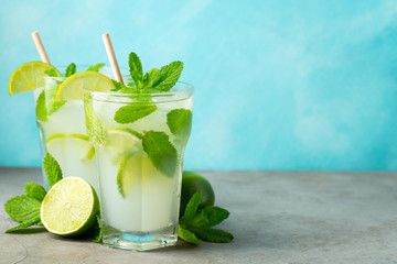 Two homemade lemonade or mojito cocktail with lime, mint and ice cubes in a glass on a light stone table. Fresh summer drink. With copy space.