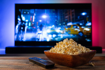A wooden bowl of popcorn and remote control in the background the TV works. Evening cozy watching a movie or TV series at home