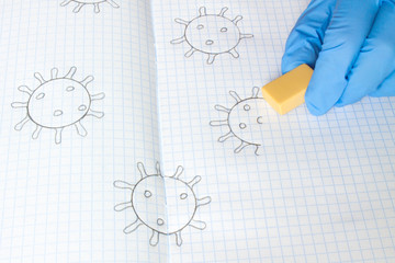 A coronavirus molecule drawn in pencil on a white notebook sheet and a hand erasing the drawing with an eraser. Concept-stop coronavirus