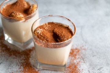Close up of a traditional Italian sweet tiramisu cake dessert in glass on grey background.