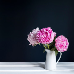 Three red peonies in a white jug on black