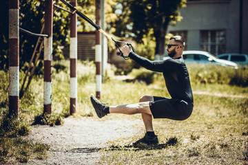 Man doing push ups exercise with trx fitness straps. Outdoor, workout, training, lifestyle concep.