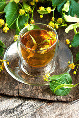 Cup of linden tea and lime flowers on  wooden table