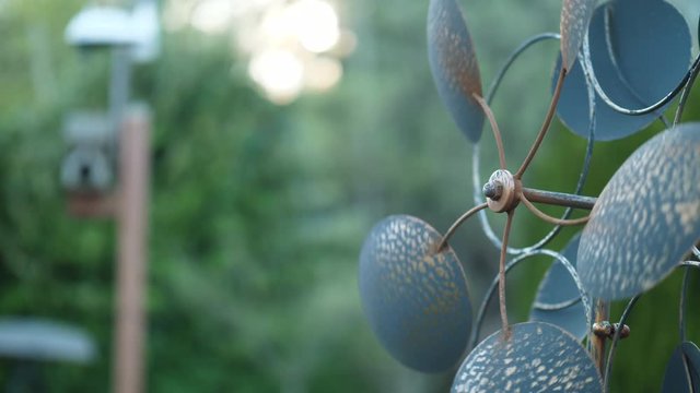 Metal pinwheel slowly spinning in the wind next to a bird house in the garden at sunset. Small strands of cobweb in-between frame. 