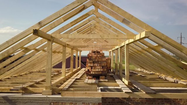 Aerial view of unfinished brick house with wooden roof frame structure under construction.