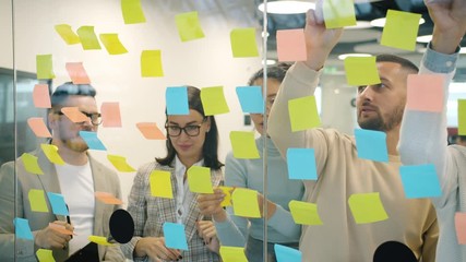 Slow motion of male and female coworkers working with colorful sticky notes brainstorming planning business in office. Meetings and job concept. - Powered by Adobe