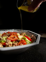 Mano de un hombre aliñando una ensalada mediterránea sobre fondo negro