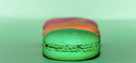 Delicious three multicolored macaroon on a green background