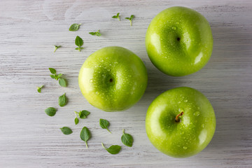 Green fresh apples and some basil leaves on wooden table close up, top view