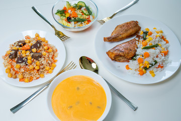 Pumpkin cream soup, fried fish with rice, pilaf and vegetable salad on a white table. Colorful food on a white background. Food concept. 