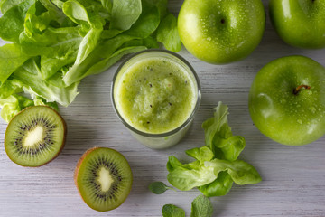 A glass of healthy green smoothie with apple, kiwi and leaves on the white wooden table