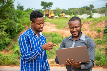 african business men, discussing and surveying a piece of land, using a laptop