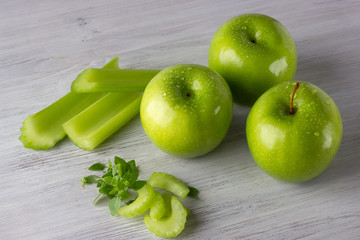 Fototapeta na wymiar Green fresh apples, celery slices and some basil leaves on wooden table close up