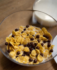 Healthy corn flakes with milk and chocolate balls in glass bowl on a wooden table. Quick breakfast concept. High angle view