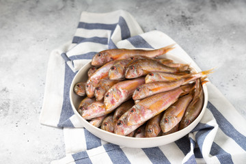 Black sea barabulka fish in a white ceramic bowl on a light gray kitchen table. A lot of fish red mullet. Black sea barabulka