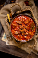 overhead shot of homemade tasty stewed meat in tomato sauce with vegetables. goulash in wooden bowl on rustic table 