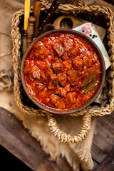 overhead shot of homemade tasty stewed meat in tomato sauce with vegetables. goulash in wooden bowl on rustic table 