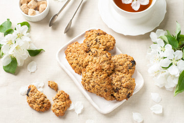 Oatmeal cookies cookies in a white ceramic plate on a light table among flowering branches. Healthy homemade oatmeal cookies. A plate of cookies and a Cup of tea on the table. The view from the top