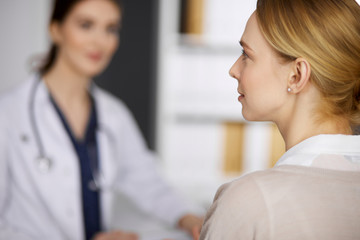 Fototapeta premium Friendly smiling female doctor and patient woman discussing current health examination while sitting in clinic. Medicine and healthcare concept