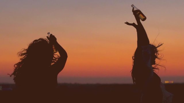 Silhouettes of partying women drinking beer against sunset sky