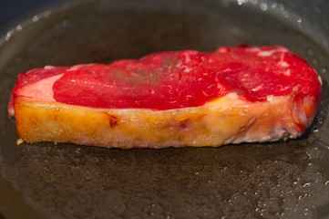 Shots of a sliced raw fresh rump  steak with fat on the steak in a pan, which the steak cooks through in high heat