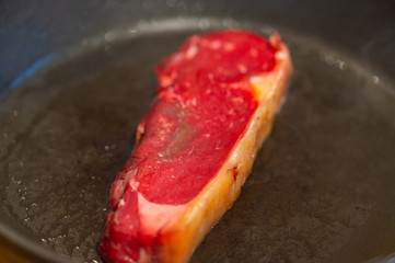 Shots of a sliced raw fresh rump  steak with fat on the steak in a pan, which the steak cooks through in high heat