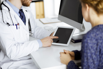 Unknown red-bearded doctor and patient woman discussing current health examination while sitting...