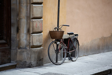 Fototapeta na wymiar Bicycle standing near wall of ancient building. Female bike with wicker basket in front is fastened with chain to post on street of European city. Wallpaper or background. Copy space at right side