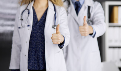 Two doctors standing with thumbs up in hospital office. Medical help, countering viral infection and medicine concept