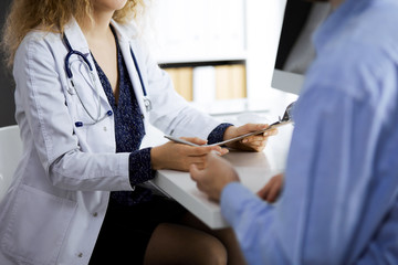 Female doctor and male patient discussing current health examination while sitting in clinic,...