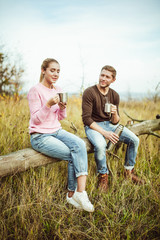 Naklejka na ściany i meble Tea party or coffee drinking outdoors. Cheerful couple drink hot coffee or tea communicate sitting on a wooden log outdoors