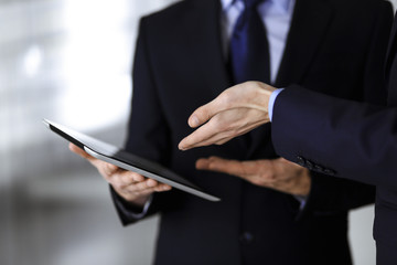 Business people use a tablet computer for discussion of their new project, standing in a modern office. Unknown businessman or male entrepreneur with a colleague at workplace. Teamwork and partnership