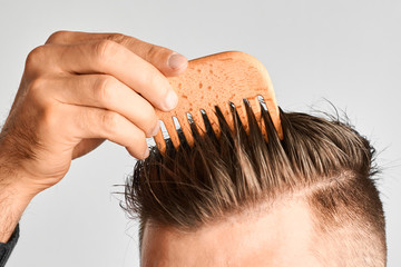 Young man styling his hair with a wooden comb. Hair styling at home. Advertising concept of shampoo...