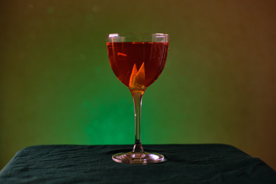 red cocktail in nick and nora glass on green background